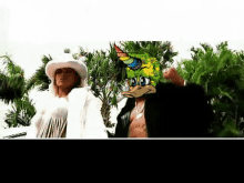 a woman in a cowboy hat stands next to a man wearing a duck mask with a rainbow horn