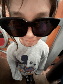 a little girl wearing sunglasses and a mickey mouse sweatshirt