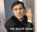 a man in a suit and tie is leaning against a wall and whispering into it .