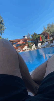 a man is laying in front of a swimming pool with an umbrella in the background