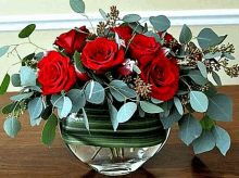 a vase filled with red roses and greenery on a wooden table .