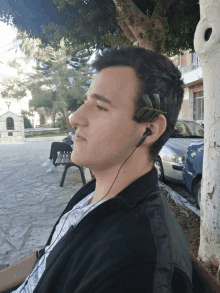 a man wearing a pair of ear buds sits under a tree in a park