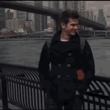 a man with a backpack stands next to a railing overlooking a body of water with a bridge in the background