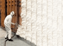 a man in a protective suit is spraying foam on a building .