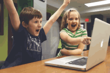 a boy and a girl are sitting at a table with a laptop and the boy is wearing a shirt that says vans