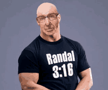 a bald man with glasses wears a black shirt that says randal 3:16