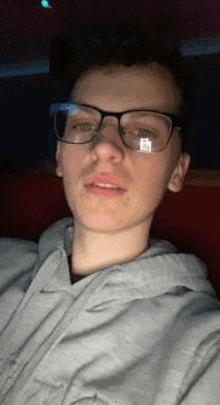 a young man wearing glasses and a gray hoodie is sitting in a car .