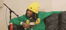 a man is sitting on a couch in front of a microphone wearing a yellow hat .