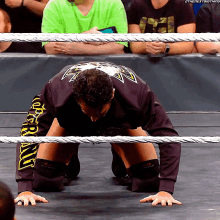 a wrestler is kneeling down in a wrestling ring with the next thing written on the bottom of his shirt