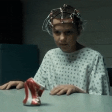 a young girl in a hospital gown is sitting at a table with a can of soda in front of her