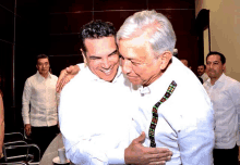 two men are hugging and one has a tie that says ' mexico ' on it