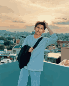 a young man standing on a rooftop holding a black bag