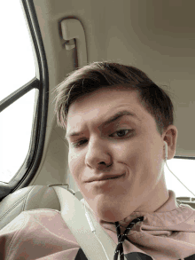 a young man wearing ear buds and a pink shirt is making a funny face in a car