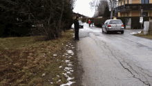 a man stands on the side of a road looking at a car with a license plate that says ' lg '