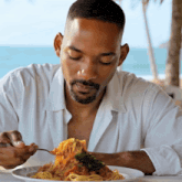 a man in a white shirt is eating a plate of spaghetti with a fork