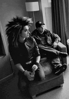 a man sitting on a couch next to a man with a mohawk