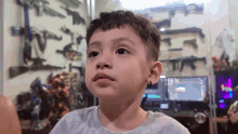 a young boy is sitting in front of a computer in a room with guns on the wall behind him .