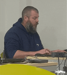 a man with a beard is sitting at a desk in front of a computer with imgplay written on the bottom