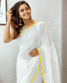 a woman wearing a white saree with a yellow border is smiling