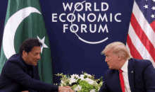 two men shaking hands in front of a world economic forum banner