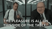 two men are sitting at a table talking to each other and one of them is holding a gun .