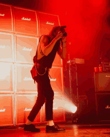 a man stands in front of a wall of marshall amps