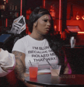 a woman wearing a shirt that says i 'm blunt because go rolled me that way sits at a table