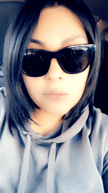 a woman wearing black sunglasses and a grey hoodie