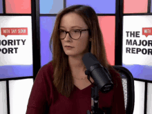 a woman wearing glasses stands in front of a microphone in front of a screen that says the major report