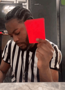 a man in a striped shirt is holding a red card in front of his face