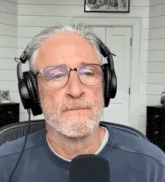 a man wearing headphones and glasses looks at the camera