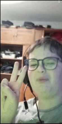 a young man wearing headphones and glasses is making a peace sign .