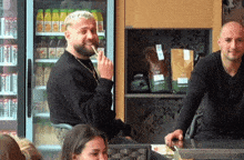 a man in a black shirt is eating a candy bar in front of a fridge full of coca cola cans