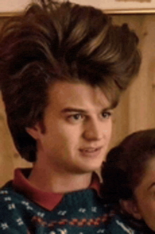 a young man with a big haircut is wearing a blue sweater .