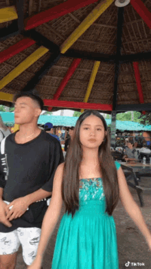 a girl in a blue dress is standing next to a man in a black shirt under a gazebo .