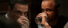 a man drinking a glass of water while another man looks on