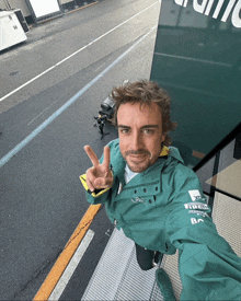 a man wearing a green jacket that says pirelli on it giving a peace sign