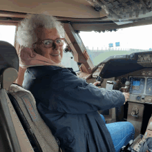 an older woman is sitting in the cockpit of an airplane with a sticker on the seat that says " emergency exit "