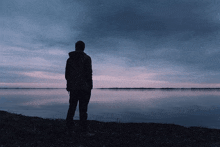 a man standing on the shore of a lake looking at the water