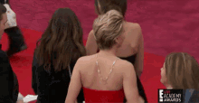 a woman in a red dress is sitting on a red carpet in front of a live academy awards sign