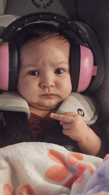 a baby wearing pink ear muffs is sitting in a car seat