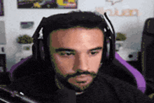 a man with a beard is wearing headphones and a microphone while sitting in a purple chair .