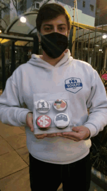 a man wearing a soulfit sweatshirt holds a box of cupcakes in his hands