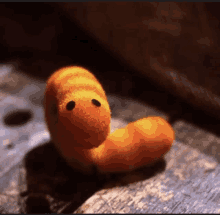 a stuffed orange worm with black eyes is on a rock