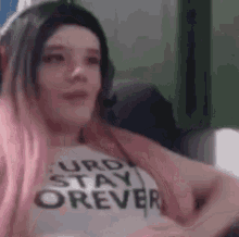 a woman with pink hair is wearing a t-shirt that says `` stay forever '' .