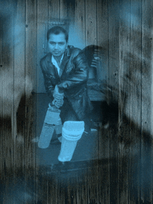 a man in a leather jacket holds a pair of slazenger cricket bats in front of a wooden wall