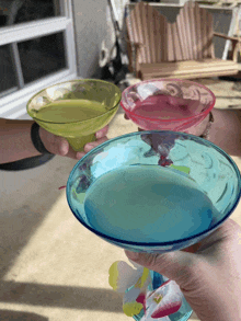 a person holding three different colored glasses of liquid