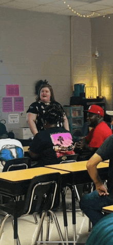 a group of people are sitting at desks in a classroom with a woman standing in front of them