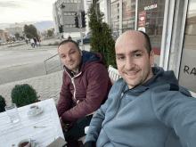 two men sit at a table in front of a building with the word siguria on it