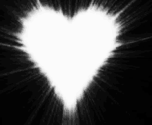 a white heart is glowing in the dark with rays coming out of it .